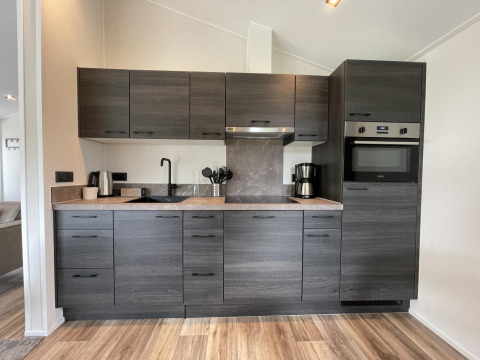 Moderne grijze keuken met ingebouwde toestellen en houten vloer in Hackfort 4 te De Utrechtse Heuvelrug, Nederland.