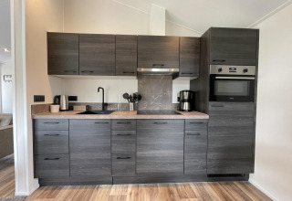 Cocina moderna gris con electrodomésticos integrados y suelo de madera en Hackfort 4 en De Utrechtse Heuvelrug, Países Bajos.