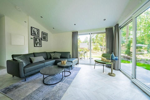 Salón moderno en la cabaña Hackfort MIVA con grandes ventanales y vistas a De Utrechtse Heuvelrug, Países Bajos.