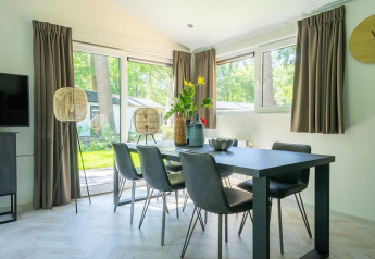 Salle à manger du lodge Hackfort MIVA avec une table moderne, six chaises et grandes baies vitrées sur la nature.