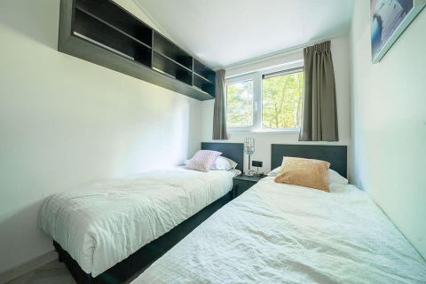 Schlafzimmer mit zwei Einzelbetten, Fenster mit Vorhängen und Wandregal in der Hackfort MIVA Lodge, Utrechtse Heuvelrug.