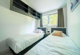 Schlafzimmer mit zwei Einzelbetten, Fenster mit Vorhängen und Wandregal in der Hackfort MIVA Lodge, Utrechtse Heuvelrug.