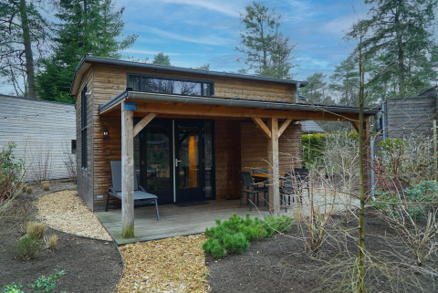 Kleines Holzhaus mit überdachter Terrasse und Gartenmöbeln bei Beekbergen, Niederlande, im Wald.