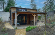 Modern tiny house with covered porch and outdoor seating, set among trees in Beekbergen, Netherlands.
