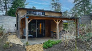 Moderne tiny house met overdekte veranda en tuinset, omgeven door bos in Beekbergen, Nederland.