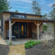 Modern tiny house with covered porch and outdoor seating, set among trees in Beekbergen, Netherlands.