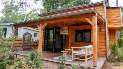 Tiny house van hout met overdekte veranda, hangstoel en tuinmeubels in Beekbergen, Nederland.