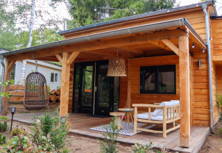 Tiny house van hout met overdekte veranda, hangstoel en tuinmeubels in Beekbergen, Nederland.