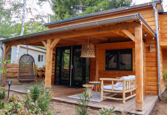 Kleines Holzhaus mit überdachter Terrasse, Hängesessel und Gartenmöbeln in Beekbergen, Niederlande.
