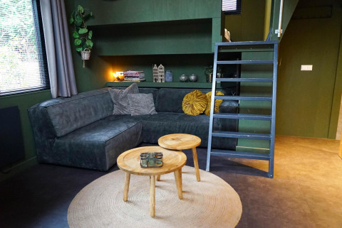 Gezellige woonkamer in Tiny House 4 Hottub te Beekbergen, Nederland, met bank, tafels en trap.