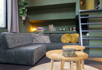 Zona giorno moderna nel Tiny House 4 Hottub a Beekbergen, Paesi Bassi, con divano verde e tavolini in legno.