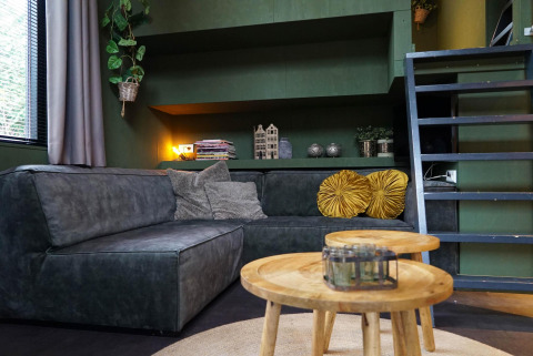 Moderne zithoek in Tiny House 4 Hottub in Beekbergen, Nederland, met groene bank en houten tafeltjes.
