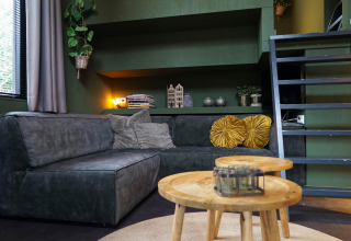 Moderne zithoek in Tiny House 4 Hottub in Beekbergen, Nederland, met groene bank en houten tafeltjes.