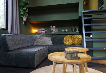 Modernes Wohnzimmer im Tiny House 4 Hottub in Beekbergen, Niederlande, mit grüner Couch und Holztischen.