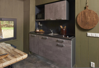 Moderne lille hus køkken med grå skabe, træbord og stort træskærebræt i Tiny House 4 Hottub, Beekbergen.