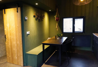Binnenzicht van een moderne tiny house met houten schuifdeur, groene muren en eethoek te Beekbergen.
