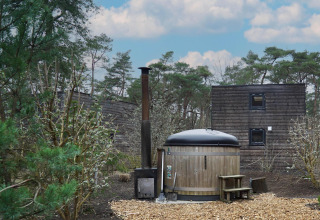 Kleines Holzhäuschen mit Hot Tub und Schornstein zwischen Bäumen in Beekbergen, Niederlande.