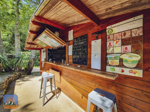 Puesto de madera con menú y taburetes en la naturaleza en Camping Des Randonneurs en Occitania, Francia.