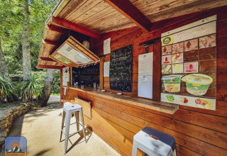 Houten kiosk met menubord en krukken in de natuur bij Camping Des Randonneurs in Occitanië, Frankrijk.