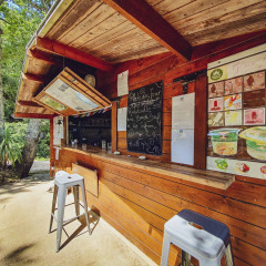 Kiosque en bois avec ardoise de menu et tabourets au Camping Des Randonneurs, Occitanie, France.