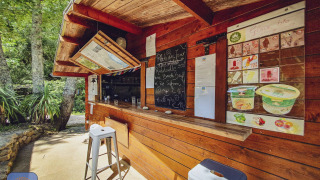 Puesto de madera con menú y taburetes en la naturaleza en Camping Des Randonneurs en Occitania, Francia.