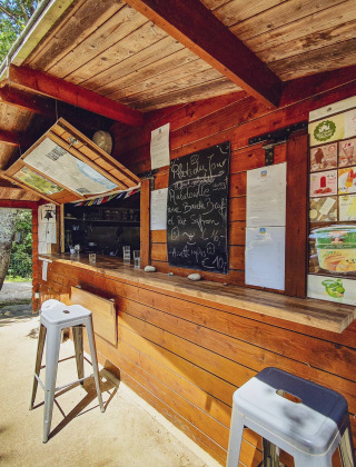 Kiosque en bois avec ardoise de menu et tabourets au Camping Des Randonneurs, Occitanie, France.