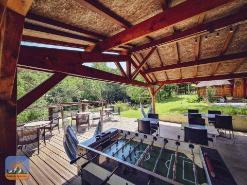 Terraza cubierta con futbolín, sillas colgantes y mesas en Camping Des Randonneurs, en Occitania, Francia.