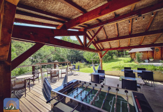 Overdekt terras met tafelvoetbal, hangstoelen en zitjes op Camping Des Randonneurs in Frankrijk.