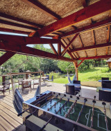 Terrasse couverte avec baby-foot, fauteuils suspendus et coin salon extérieur au Camping Des Randonneurs.