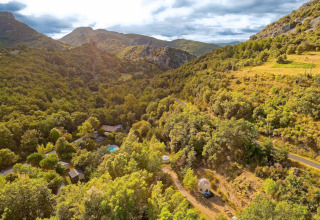 Aerial view of the lush, mountainous landscape near Fenouillet, Occitanie, France, with cabins among trees.