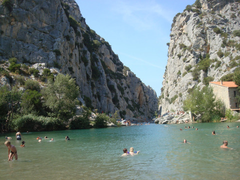 Camping Des Randonneurs en Occitania, Francia, con personas nadando en un río rodeado de altos acantilados.