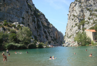 Camping Des Randonneurs en Occitanie, France, avec des vacanciers nageant dans une rivière entourée de falaises.