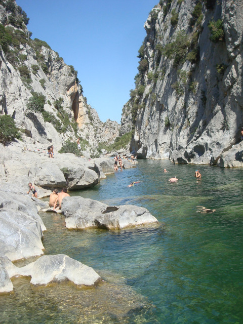 People swimming and relaxing by a rocky river near Fenouillet, Occitanie, France, on a sunny day.