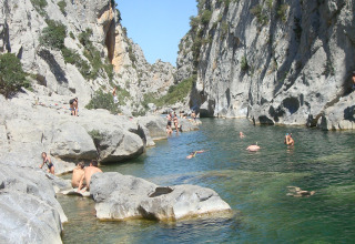 People swimming and relaxing by a rocky river near Fenouillet, Occitanie, France, on a sunny day.