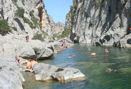 Personas bañándose y descansando en un río rocoso cerca de Fenouillet, Occitania, Francia, bajo el sol.
