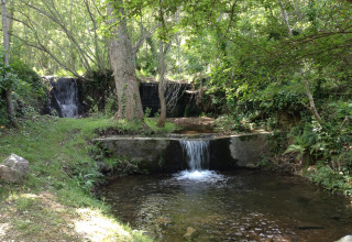 Klein watervalletje in Camping Des Randonneurs, een vakantiepark in Occitanië, Frankrijk, tussen groen.