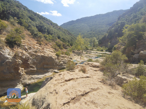 Scenic rocky valley with lush hills and river near Camping Des Randonneurs in Occitanie, France.