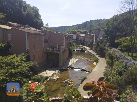 Vista de un río, edificios antiguos y flores en Camping Des Randonneurs, parque vacacional en Occitania, Francia.
