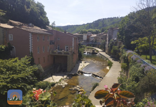 Blick auf einen Fluss, alte Gebäude und Blumen im Camping Des Randonneurs in Occitanie, Frankreich.