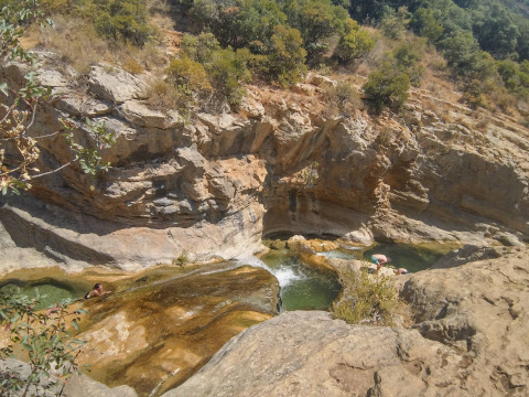 Persone che nuotano e si rilassano nelle piscine naturali di roccia a Camping Des Randonneurs, Occitania, Francia.