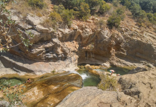 Persone che nuotano e si rilassano nelle piscine naturali di roccia a Camping Des Randonneurs, Occitania, Francia.