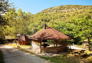 Camping Des Randonneurs in Occitanië, Frankrijk, met grillhut, picknickbanken en bosrijke heuvels rondom.