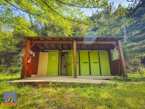 Edificio de servicios exteriores con puertas verdes en un glamping rodeado de bosque y naturaleza.