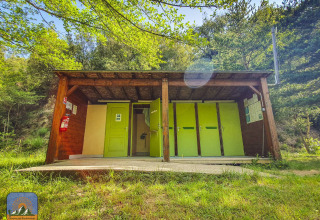 Edificio de servicios exteriores con puertas verdes en un glamping rodeado de bosque y naturaleza.