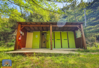 Udendørs facilitetsbygning med grønne døre på en glampingplads omgivet af natur og sollys.