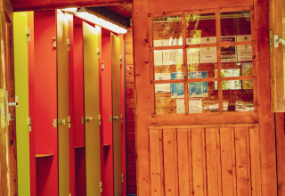 Entrée d’une cabane en bois avec portes ouvertes, révélant des cabines de toilettes colorées en glamping.