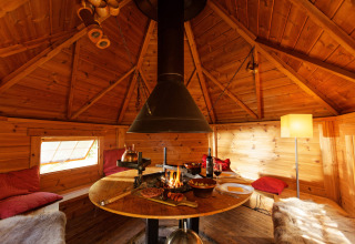 Knusse houten hut op Camping Des Randonneurs in Occitanië, Frankrijk, met centrale open haard en zithoek.