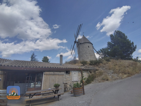 Foto de un molino de viento y un edificio bajo un cielo azul en Camping Des Randonneurs, Occitania, Francia.