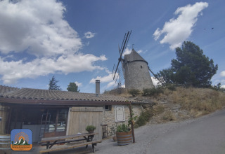 Afbeelding van een windmolen en gebouw onder een blauwe lucht bij Camping Des Randonneurs in Occitanië, Frankrijk.