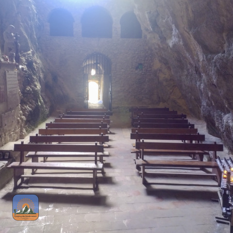 Stone benches inside a cave chapel near Fenouillet, Occitanie, France, with sunlight at the entrance.